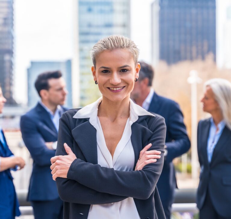 Caucasian businesswoman in a professional suit stands in front of a group of businesspeople