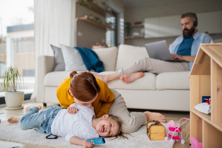 Mother with daughter playing indoors at home, everyday life and home office with child concept.